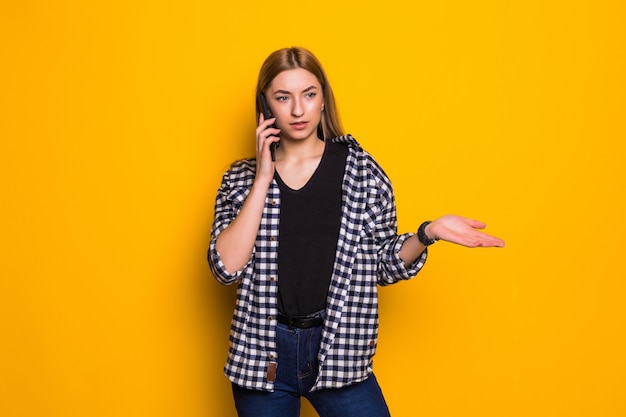 Confundida joven mujer con sobrepeso que se encuentran aisladas sobre la pared amarilla, hablando por teléfono móvil