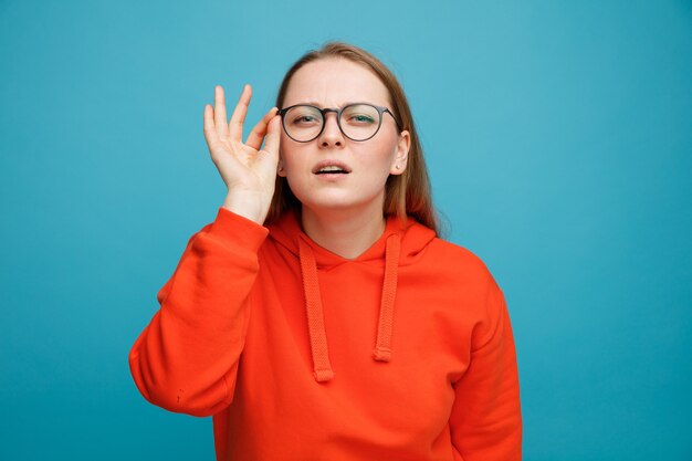 Confundida joven rubia vistiendo y agarrando gafas