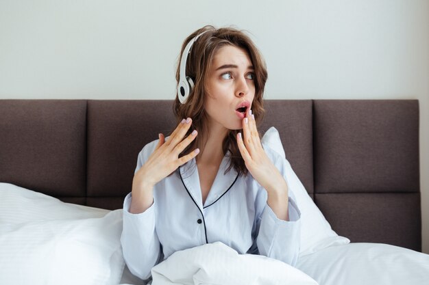 Confundida jovencita vestida con pijama escuchando música.