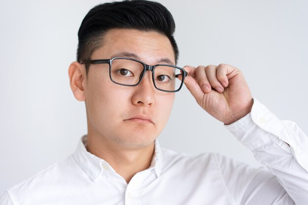 Confundido hombre asiático ajustando gafas