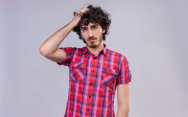 Un confundido joven apuesto con el pelo rizado en camisa a cuadros con la mano en el cabello