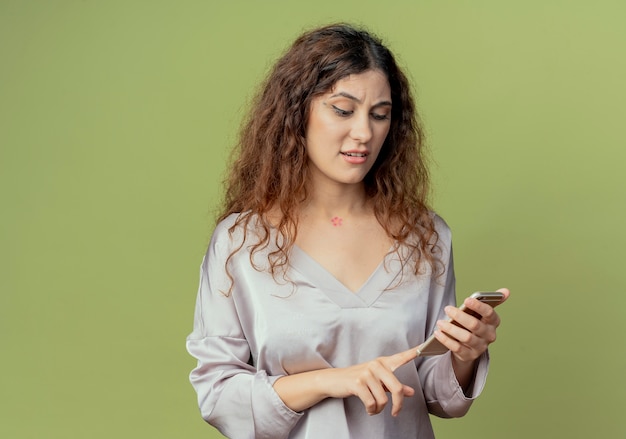 Confundido joven bastante mujer oficinista marcar el número en el teléfono aislado en la pared verde oliva