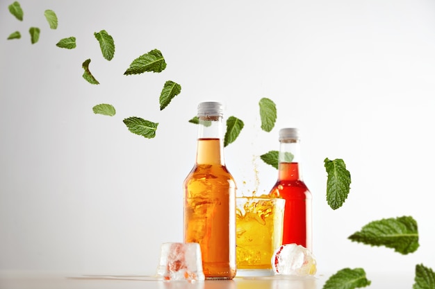 Foto gratuita congelado en salpicaduras de aire de cóctel de cubito de hielo en vaso con bebida sabrosa amarilla entre dos botellas transparentes selladas sin etiqueta con aperol y sidra