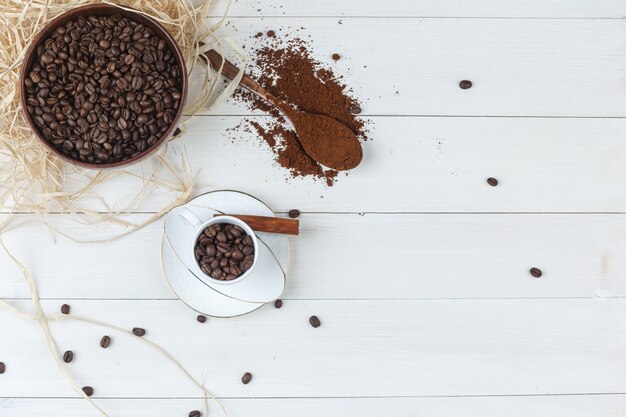 Conjunto de café molido, canela en rama y granos de café en un tazón y taza sobre un fondo de madera. vista superior.