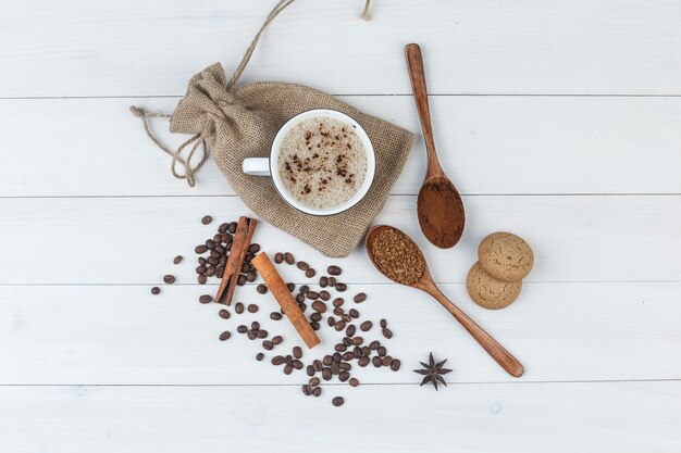 Conjunto de café molido, especias, granos de café, galletas y café en una taza sobre fondo de madera y saco. vista superior.