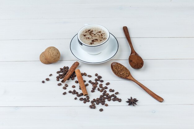 Conjunto de café molido, especias, granos de café, galletas y café en una taza sobre un fondo de madera. vista de ángulo alto.