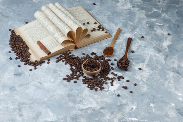 Conjunto de café molido, libro, canela en rama y granos de café en un tazón y cuchara de madera sobre un fondo gris sucio. vista de ángulo alto.