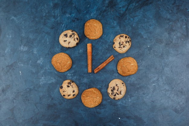 Conjunto de canela y diferentes tipos de galletas sobre un fondo azul oscuro. endecha plana.