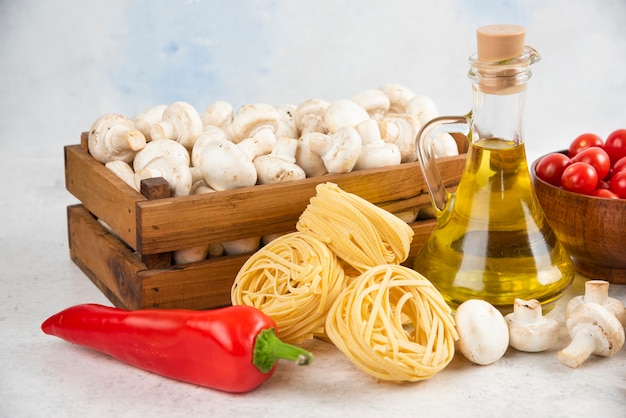 Conjunto de champiñones, aceite de oliva virgen extra, pastas, tomates cherry y guindillas sobre una pieza de mármol.