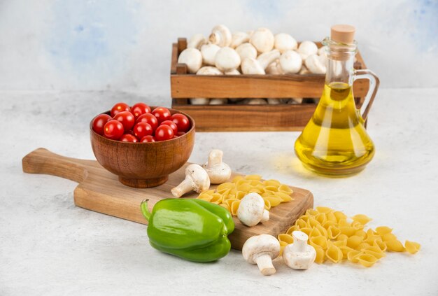 Conjunto de champiñones, aceite de oliva virgen extra, pastas, tomates cherry y guindillas sobre una pieza de mármol.