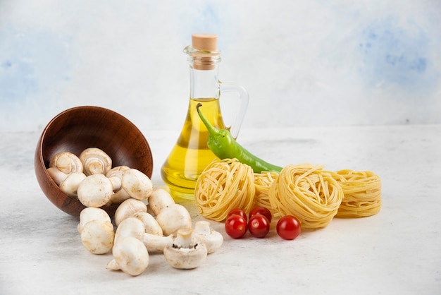 Foto gratuita conjunto de champiñones, aceite de oliva virgen extra, pastas, tomates cherry y guindillas sobre una pieza de mármol.