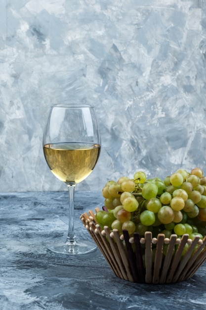 Conjunto de una copa de vino y uvas verdes en una canasta sobre un fondo de yeso sucio. vista lateral.