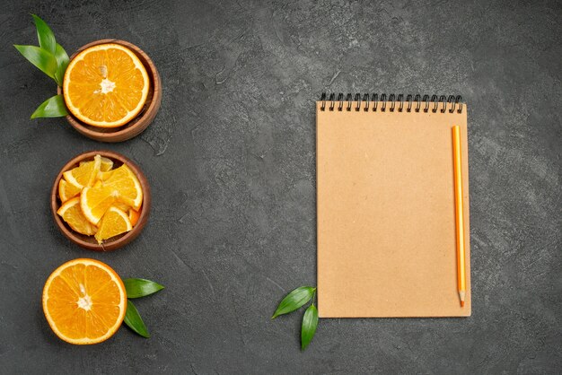 Conjunto de cortar por la mitad en rodajas en trozos de hojas de naranja fresca y cuaderno sobre mesa negra