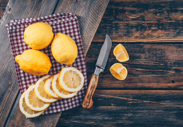 Conjunto de cuchillo, rodajas y limones sobre un fondo oscuro de la madera. aplanada