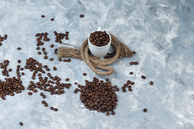 Conjunto de cuerdas y granos de café en una taza sobre un fondo de mármol azul. vista de ángulo alto.