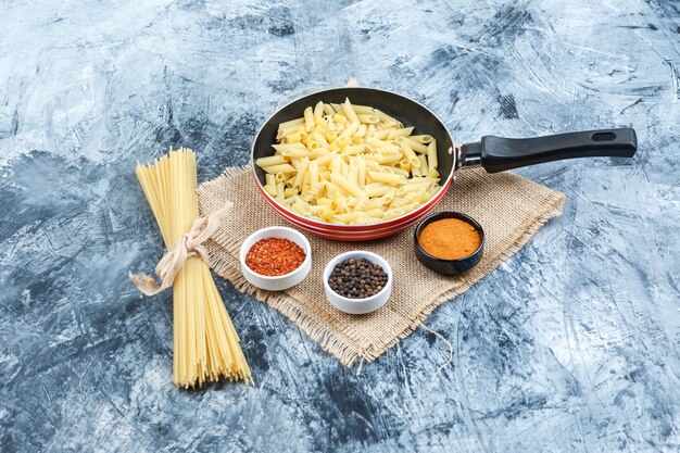 Conjunto de especias y pasta cruda en una sartén sobre yeso y un pedazo de fondo de saco. vista de ángulo alto.