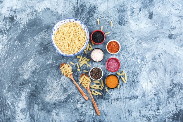 Conjunto de especias y pasta fusilli en un tazón y cucharas de madera sobre un fondo de yeso gris. vista superior.