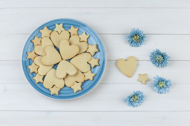 Conjunto de flores y galletas en un plato sobre un fondo de madera. endecha plana.