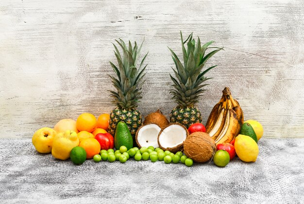 Conjunto de frutas de plátanos, piñas, cocos, aguacates, membrillos, duraznos, naranjas, ciruelas verdes, limones en grunge gris y pared de madera. vista lateral.