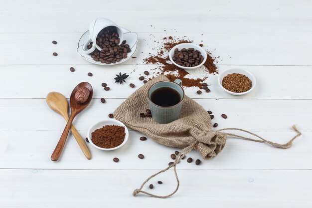 Conjunto de granos de café, café molido, cucharas de madera y café en una taza sobre fondo de madera y saco. vista de ángulo alto.