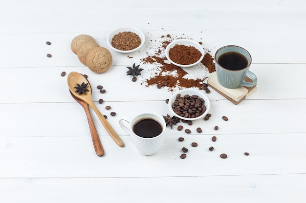 Conjunto de granos de café, café molido, especias, galletas, cucharas de madera y café en tazas sobre un fondo de madera. vista de ángulo alto.