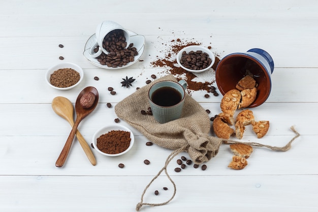 Conjunto de granos de café, café molido, galletas, cucharas de madera y café en una taza sobre fondo de madera y saco. vista de ángulo alto.