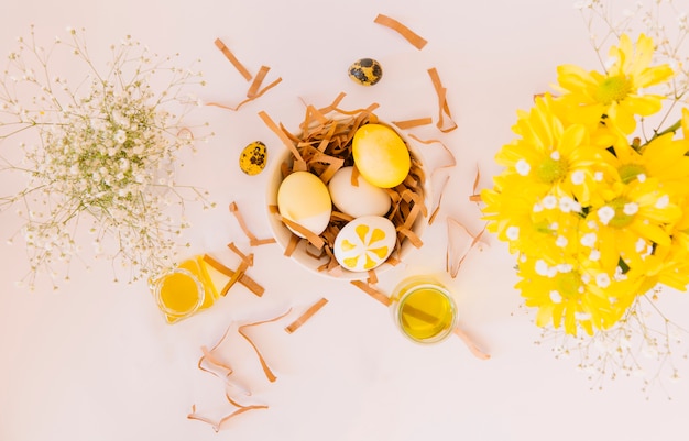 Conjunto de huevos de Pascua amarillos en un tazón entre flores frescas y latas de líquido colorante