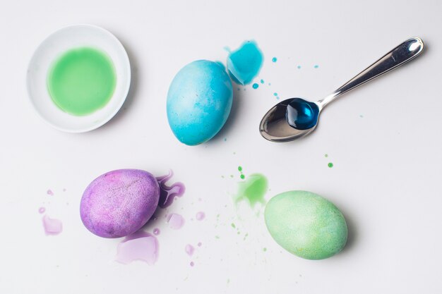 Conjunto de huevos de Pascua brillantes entre manchas, cuchara y tinte líquido.