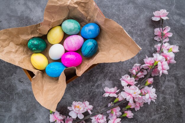 Conjunto de huevos de Pascua brillantes en papel artesanal en un tazón cerca de ramita de flor