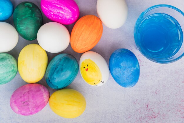 Conjunto de huevos de pascua con dibujo junto a vaso de agua.