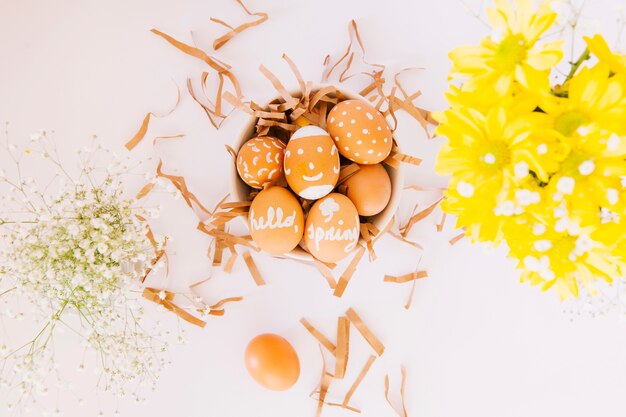 Conjunto de huevos de Pascua naranja en un tazón entre flores frescas