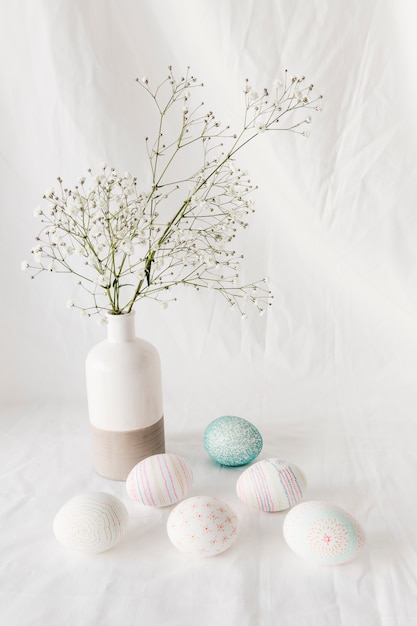 Conjunto de huevos de Pascua con patrones cerca de ramita de planta en florero