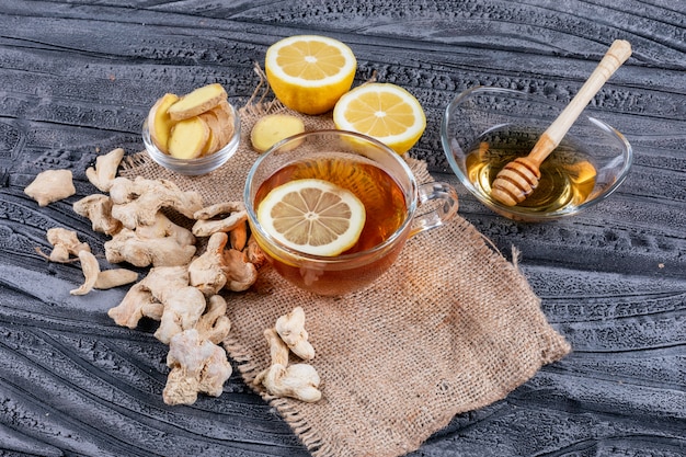 Conjunto de jengibre, limón y miel y un té en tela de saco y fondo de madera oscura. Vista de ángulo alto.