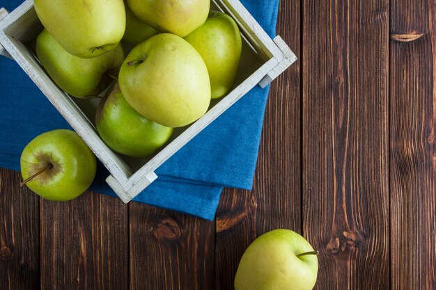 Conjunto de jugo de manzana y manzanas verdes en una caja de madera sobre un paño y fondo de madera. aplanada espacio para texto