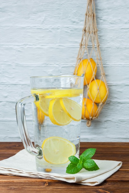 Foto gratuita conjunto de limones, hojas y jarra de limón sobre una superficie de madera y blanca. vista lateral. espacio para texto