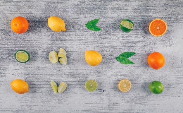 Conjunto de limones verdes y amarillos y naranja con rodajas sobre un fondo de madera gris. vista superior.