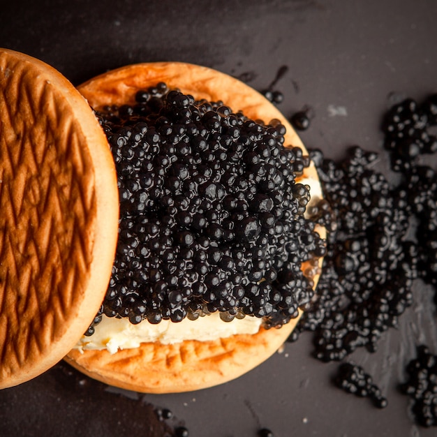 Conjunto de mantequilla y caviar negro entre galletas sobre un fondo oscuro. vista superior.