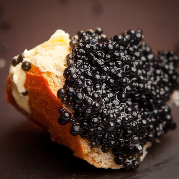 Conjunto de mantequilla y caviar negro sobre un pan sobre fondo oscuro. Vista de ángulo alto.