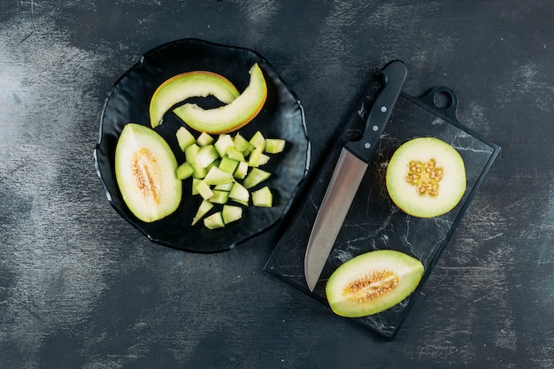 Conjunto de melón y cuchillo y melón en rodajas en un recipiente negro sobre un fondo oscuro de la madera. aplanada