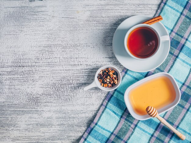 Conjunto de miel y té de hierbas y una taza de té en un paño de picnic y fondo de madera gris. vista superior. espacio para texto