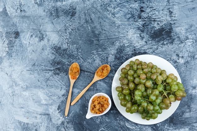 Conjunto de pasas y uvas verdes en un plato blanco sobre un fondo de yeso sucio. vista superior.