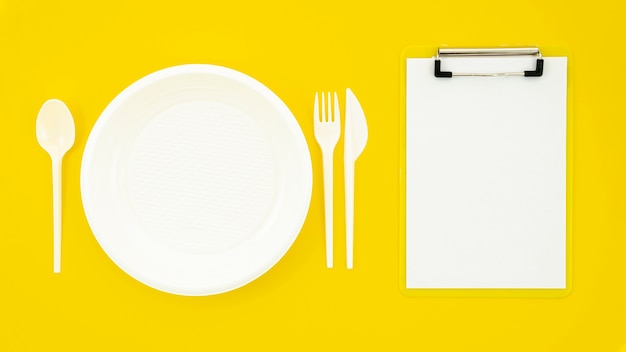 Conjunto de plato blanco y portapapeles sobre fondo amarillo