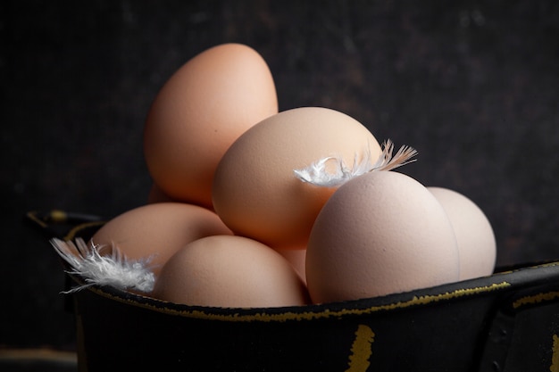 Conjunto de plumas y huevos en una olla sobre un fondo oscuro de la madera. de cerca.