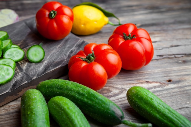 Conjunto de rodajas de pepino, ajo, limón y tomate en una tabla de cortar sobre un fondo oscuro de la madera. Vista de ángulo alto.