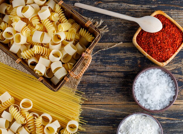 Conjunto de sal, especias rojas, espaguetis y pasta de macarrones sobre un fondo de madera. aplanada
