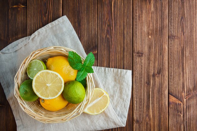 Conjunto de tela blanca y limones en una canasta sobre un fondo de madera. vista superior.