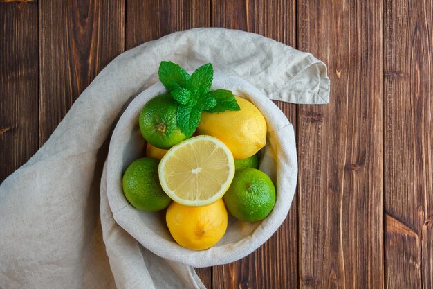 Conjunto de tela blanca, la mitad de limón y limones en una canasta sobre una superficie de madera. vista superior.