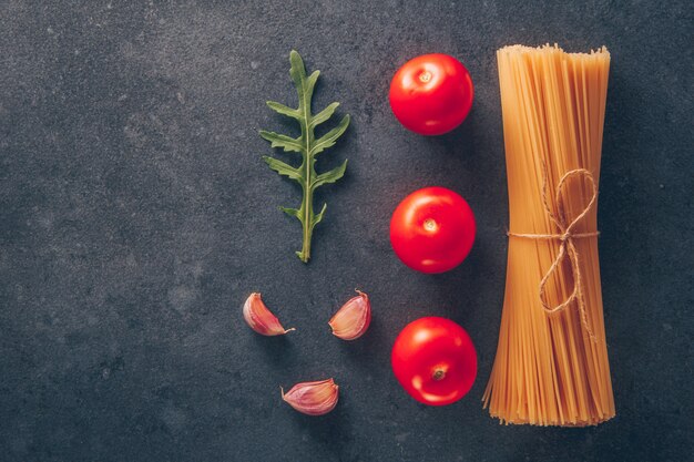 Conjunto de tomates y ajo y pasta de espagueti sobre un fondo gris con textura. vista superior. espacio para texto