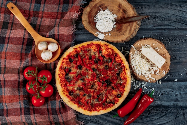 Conjunto de tomates, pimientos, champiñones, queso y harina y pizza sobre un fondo de tela de madera oscura y picnic. aplanada