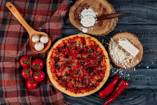 Conjunto de tomates, pimientos, champiñones, queso y harina y pizza sobre un fondo de tela de madera oscura y picnic. aplanada